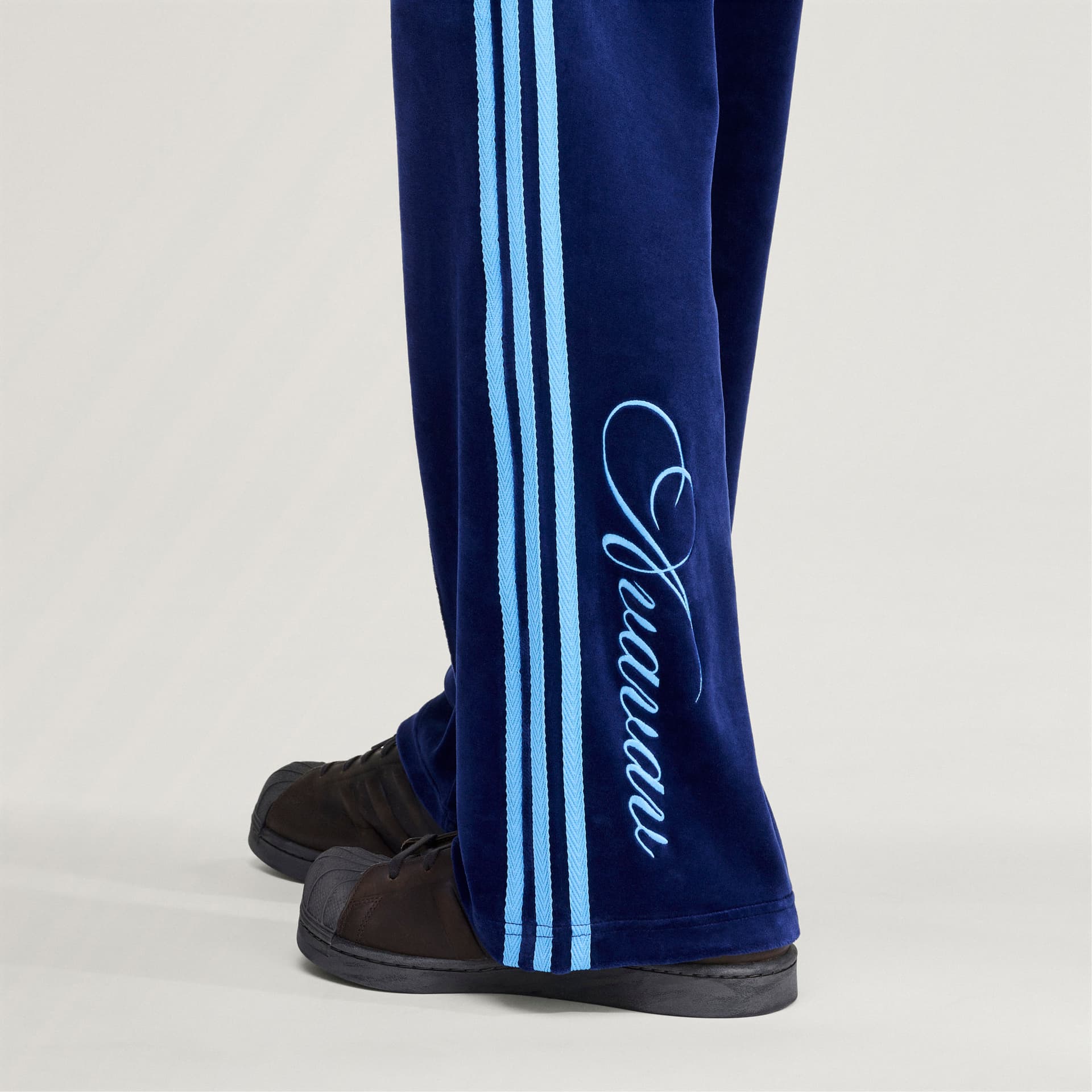 Close-up detail of the adidas Originals by Avavav Velvet Track Pant in blue, showing the light blue stripes and script logo.