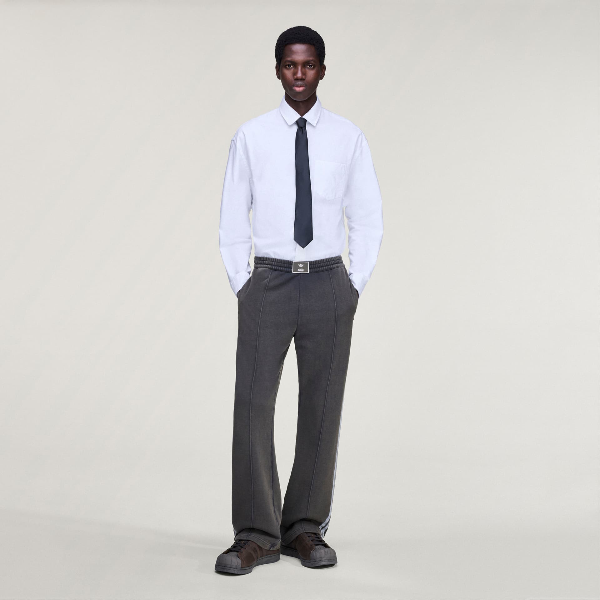 A model styles the grey adidas Originals by Avavav French Terry Track Pant with a formal white shirt and black tie.