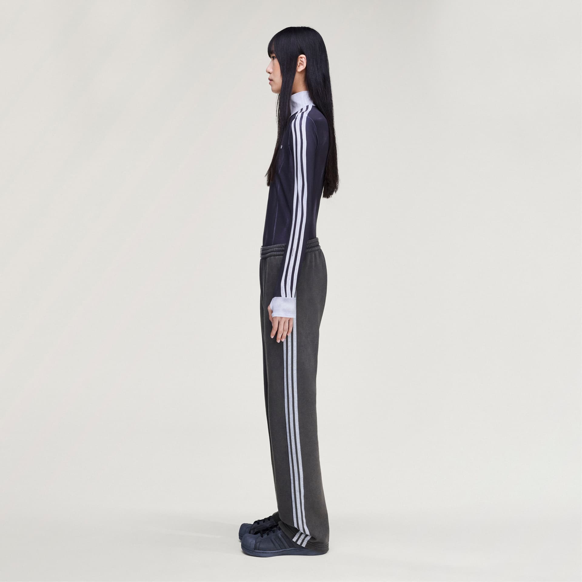 Side profile of a model wearing adidas Originals by Avavav French Terry Track Pants in dark grey with signature side stripes.