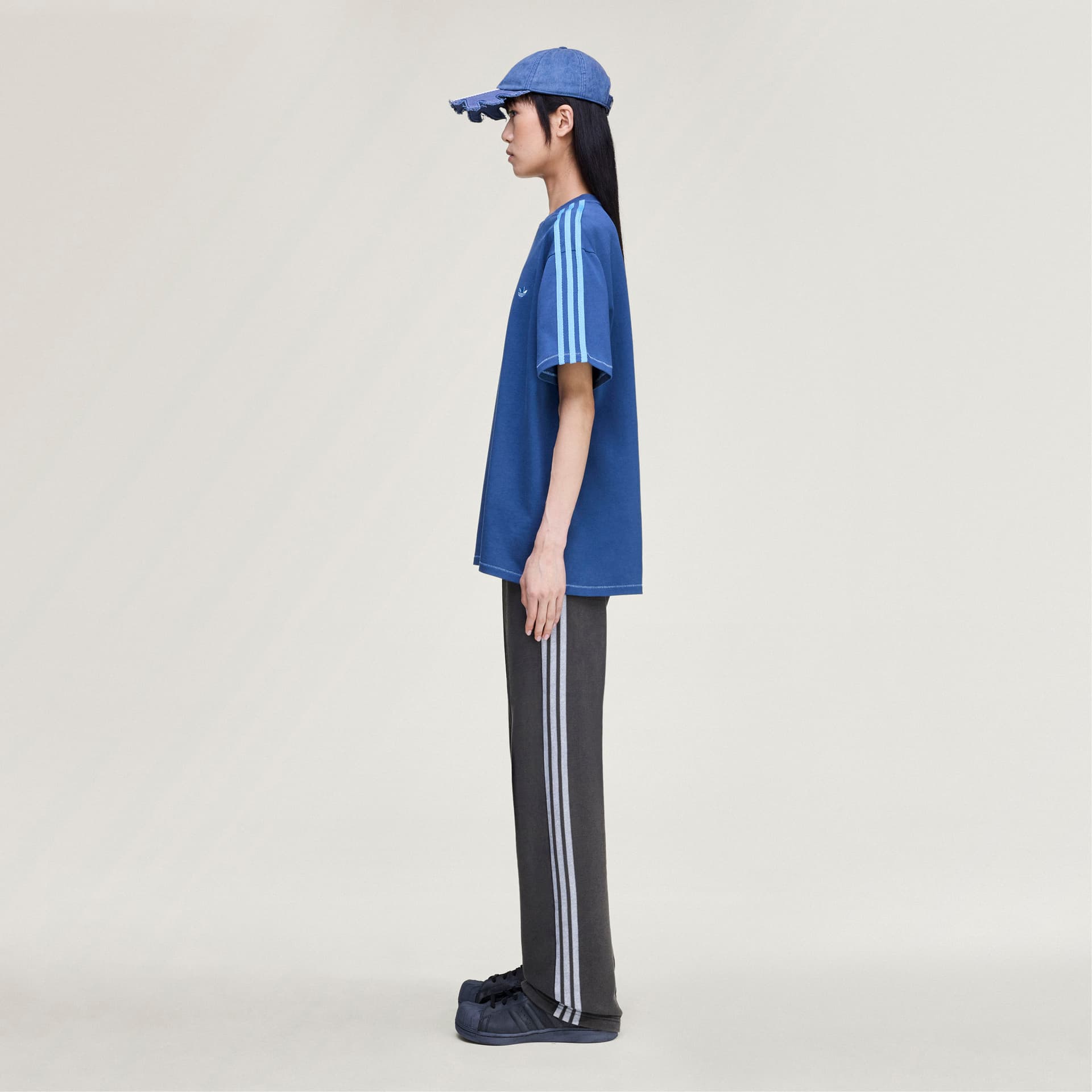 Side view of a model wearing the blue adidas Originals by Avavav T-shirt with light blue stripes on the sleeve.
