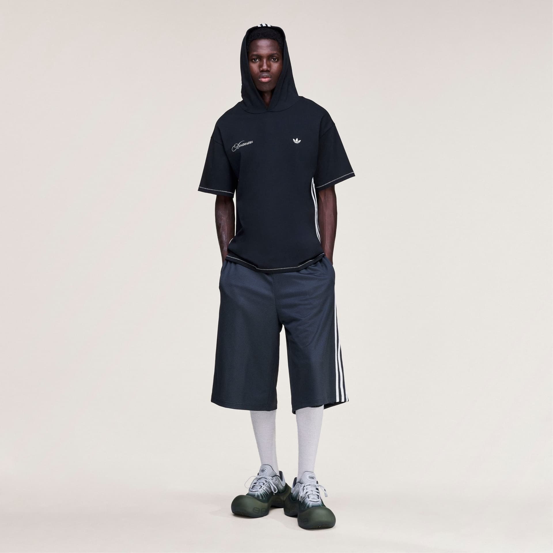 A model stands front-on wearing the adidas Originals by Avavav hooded t-shirt in black, with the hood up.