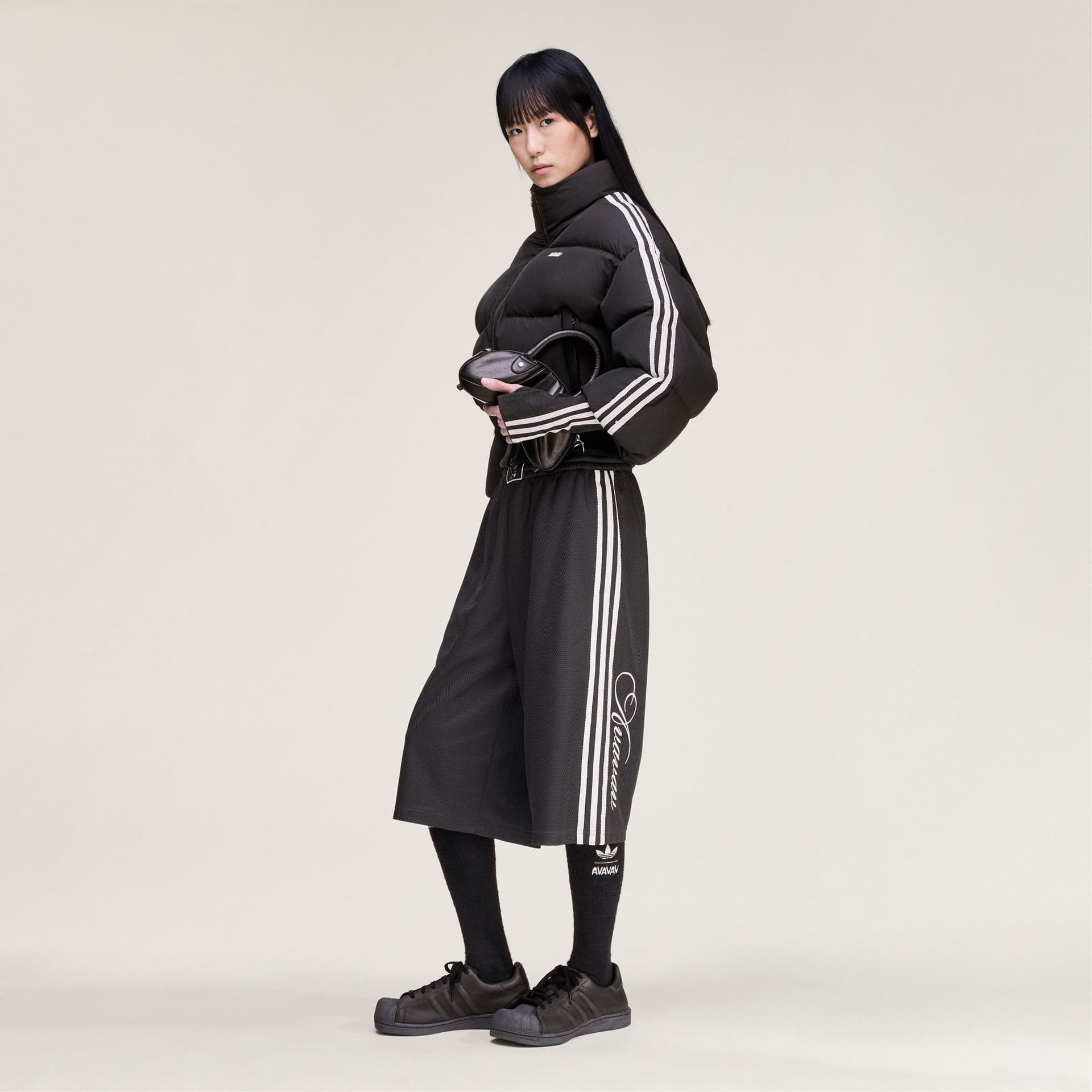 Side profile of a model wearing the black adidas Originals by Avavav basketball shorts with a matching cropped puffer jacket.