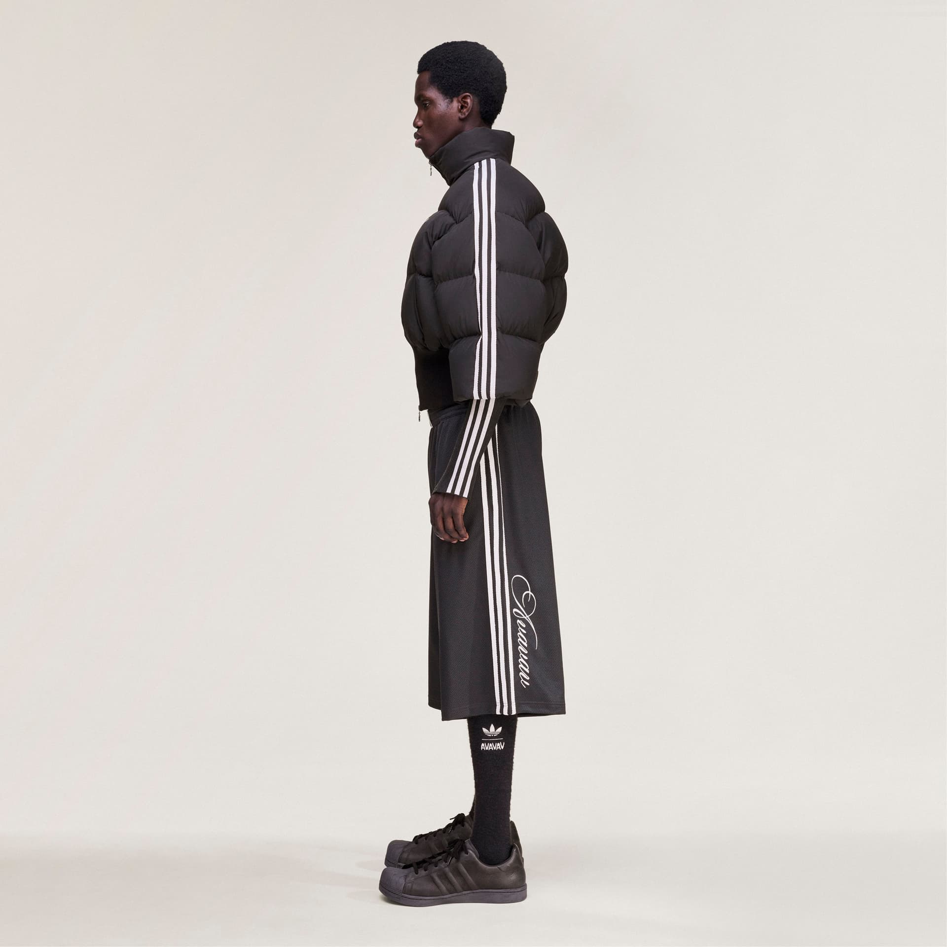 Side profile of a model wearing the black adidas Originals by Avavav basketball shorts, featuring white side stripes.