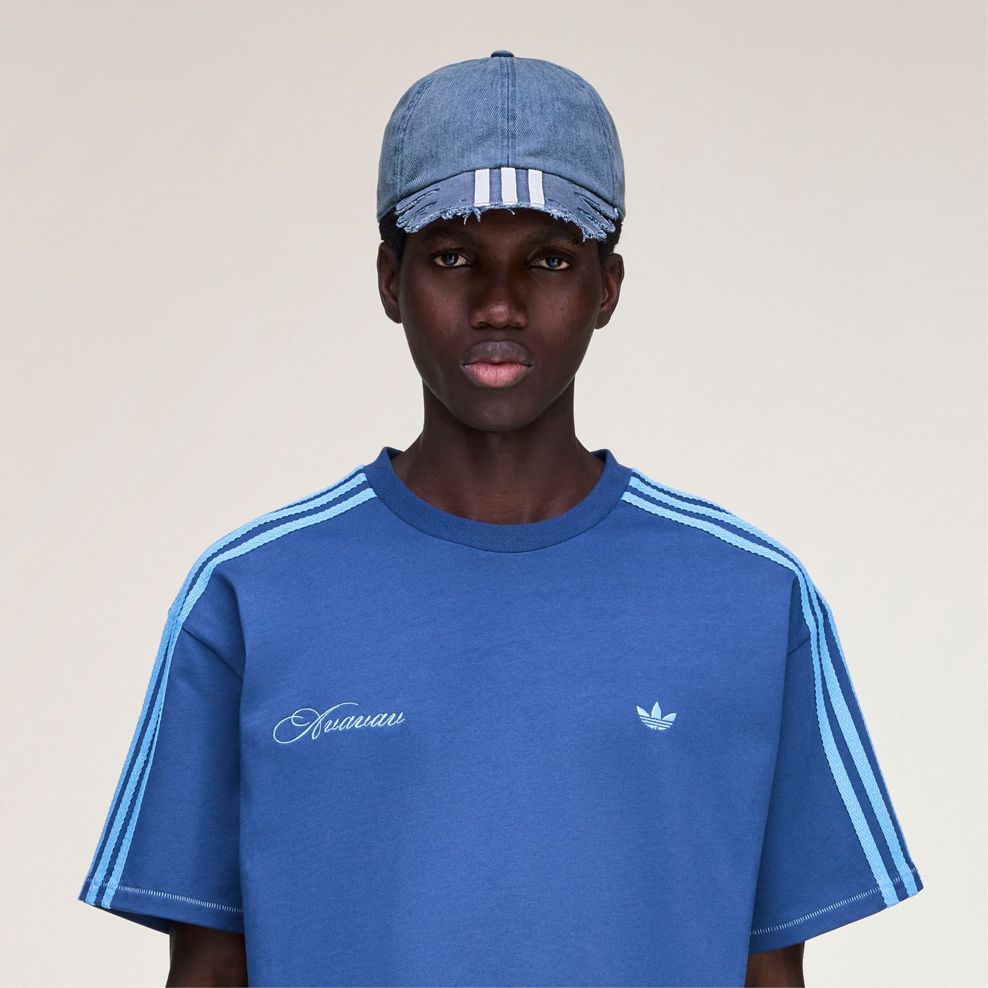 Front view of a model wearing the blue adidas Originals by Avavav Slashed Cap, featuring a raw-edge brim with three stripes.