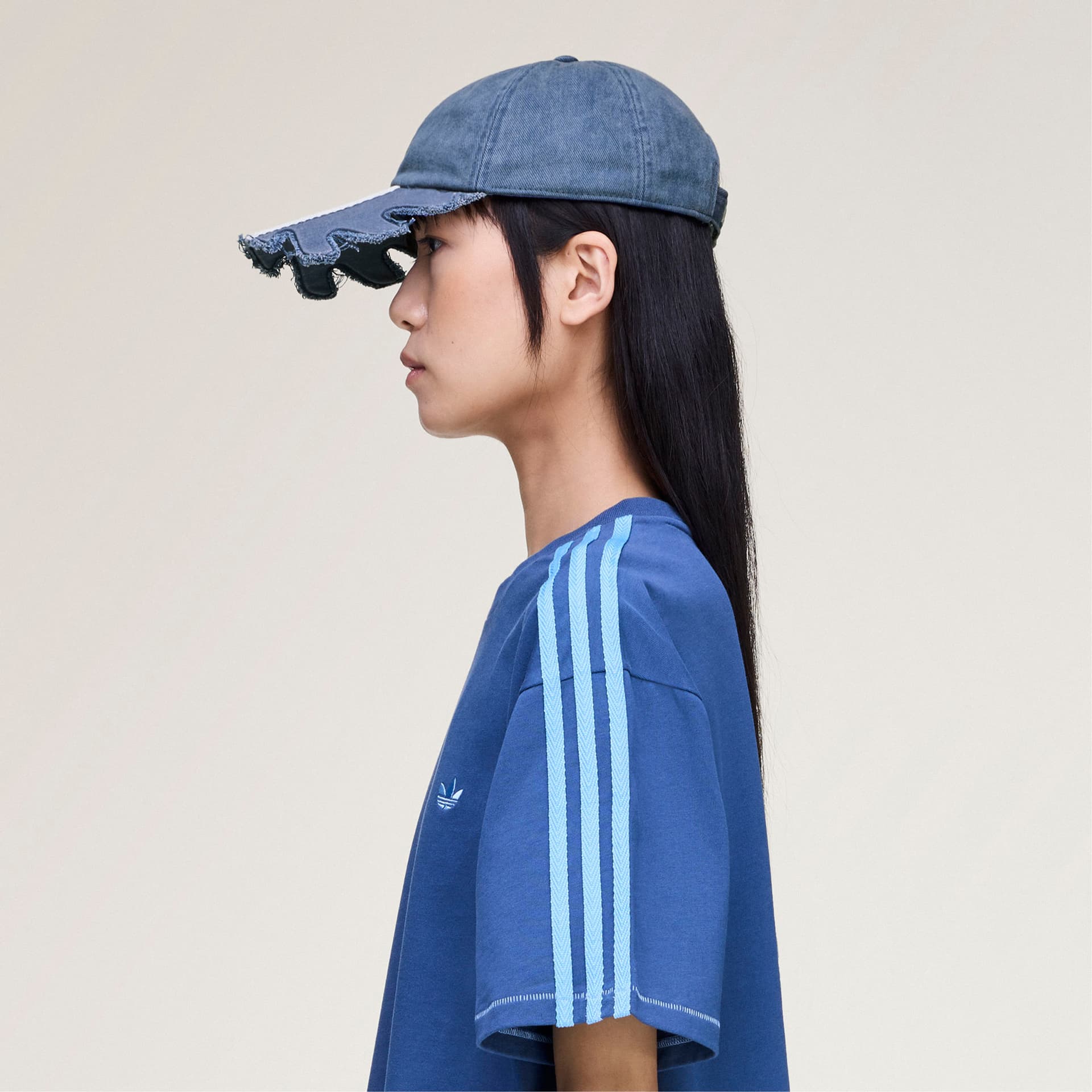 Side profile of a model wearing the blue adidas Originals by Avavav Slashed Cap with a raw-edge cutout brim.