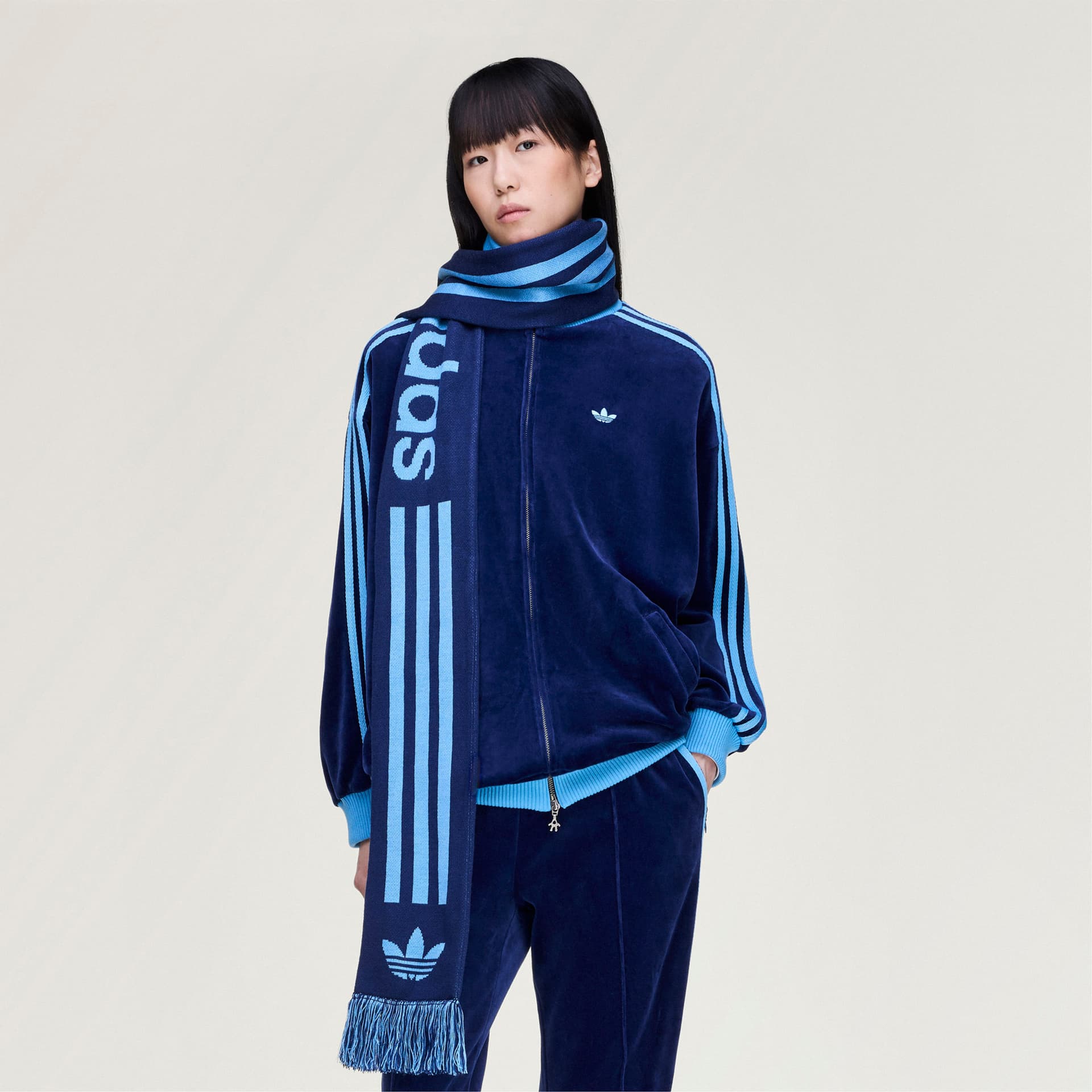 A model wears the adidas Originals by Avavav Scarf in navy and light blue, styled with a matching velour tracksuit.
