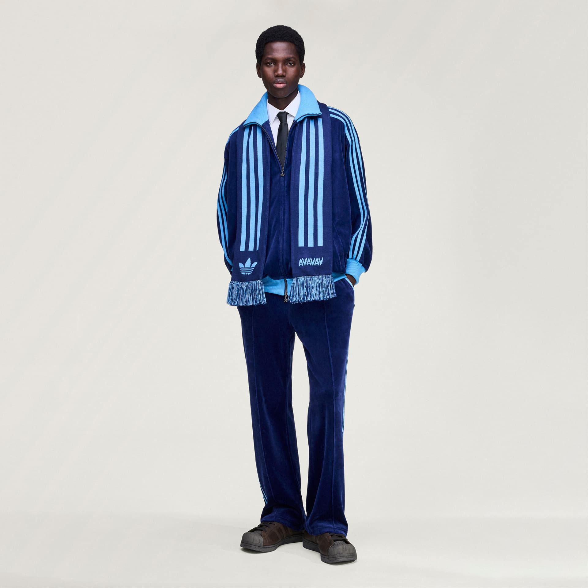 A model, seen from the front, wears the adidas Originals by Avavav blue striped scarf with a matching dark blue tracksuit.