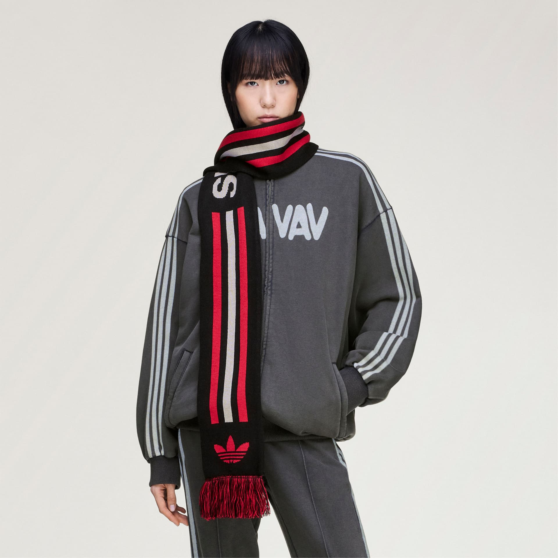 Front view of a model wearing the adidas Originals by Avavav Scarf in black, red & white stripes with a matching tracksuit.